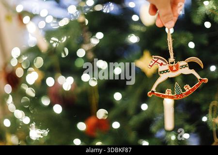 Hand hält weihnachtspferd Spielzeug auf dem Hintergrund des weihnachtsbaums mit goldenen Lichtern. Symbol 2026. Frohes Neues Jahr! Kopierbereich Stockfoto