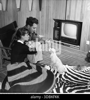 Fernsehgerät in den 1950ern Ein früheres Fernsehgerät, das nur Fernsehsendungen in Schwarzweiß anzeigen kann. Mit den Knöpfen an der Vorderseite steuern Sie Bild und Ton. Gunwer Bergkvist, eine schwedische Schauspielerin, geboren am 3. August 1932. Hier zu Hause bei ihrem Ehemann, dem Regisseur Hans Lagerkvist, 1957. Bei dem Fernseher handelt es sich um ein Philips Gerät, dessen Testkarte leicht auf dem Bildschirm sichtbar ist. Auf dem Boden liegt eine Zebrahaut. Stockfoto