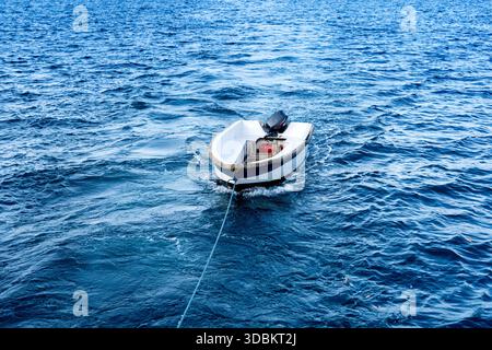 Kleine motorisierte Schlauchbootpfade sanft auf dem offenen Meer, gebunden und treiben durch plätschernde blaue Wellen unter klarem Himmel. Stockfoto