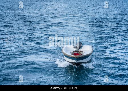 Kleine motorisierte Schlauchbootpfade sanft auf dem offenen Meer, gebunden und treiben durch plätschernde blaue Wellen unter klarem Himmel. Stockfoto