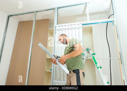 Handyman cutting metal profiles for installing plasterboard walls in a house undergoing renovation, using metal studs and tracks to ensure precision in construction and design Stockfoto
