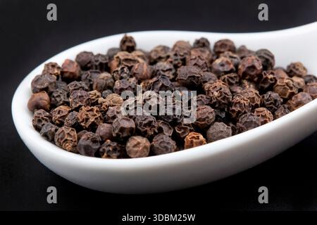 Pfefferkörner in weißen Löffel am schwarzen Tisch Stockfoto