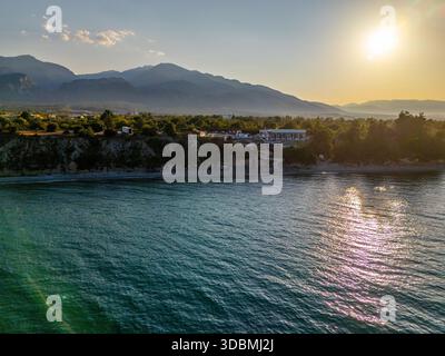 Aus der Vogelperspektive auf die Sonne, die das türkisfarbene Meer küsst, während es auf die zerklüftete Küste unter den majestätischen Bergen trifft, Litochoro, Pieria, Griechenland. Stockfoto
