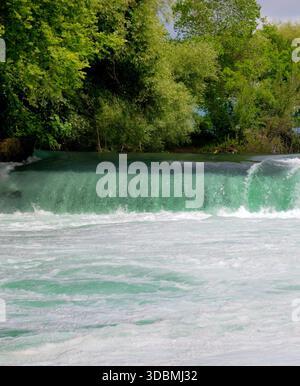 Der mächtige türkisfarbene Manavgat Wasserfall fließt anmutig, umgeben von üppigen grünen Bäumen unter hellem Himmel. Stockfoto