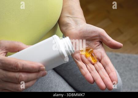 Seniorenhände, die goldene Kapseln aus weißem Pillengefäß gießen. Gesundheit im Erwachsenenalter, Erhaltung von Aktivität und Energie. Krankheitsprävention, Vitamineinsatz und Stockfoto