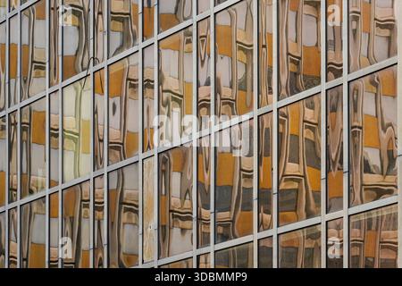Retro-Reflexionen: Abstraktes Mosaik. In Lyon, Frankreich, spiegelt eine Glasfassade den Geist der 1970er Jahre in verzerrten Mustern und gedämpften Farbtönen wider und bildet ein abstraktes Mosaik aus Vergangenheit und Gegenwart. Stockfoto