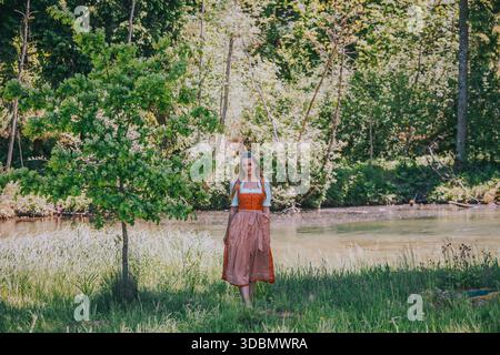Eine junge Frau mit langen blonden Haaren, gekleidet in einem traditionellen roten Dirndl mit einer weißen Bluse und einer roten Schürze Stockfoto
