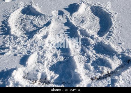 Im Schnee entsteht ein Schneeengel mit Flügeln aus Schnee. Der Engel ist sehr detailliert und hebt sich im Schnee hervor Stockfoto
