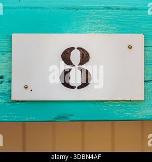 Nummer acht auf einer weißen Platte, befestigt an einer Holzplatte, Hausnummernschild. Stockfoto