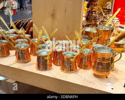 Türkische Kupferkaffeekannen auf Holzregal im Souvenirshop. Traditionelle Kaffeezubereitung, Metallhandwerkskunst, kulturelles Ritual Stockfoto