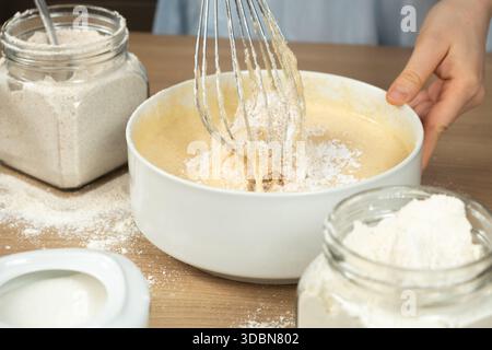 Nahaufnahme von weiblichen Händen, die dicken Batter nach dem Hinzufügen von Mehl in eine weiße Schüssel rausquetschen. Stockfoto