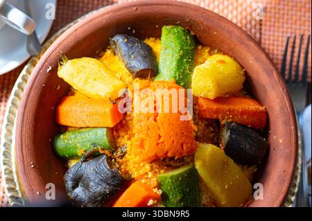 Nahaufnahme eines traditionellen marokkanischen Couscous, serviert in einer rustikalen Tonschale, garniert mit bunt gedämpftem Gemüse. Ein lebendiges und authentisches Repre Stockfoto