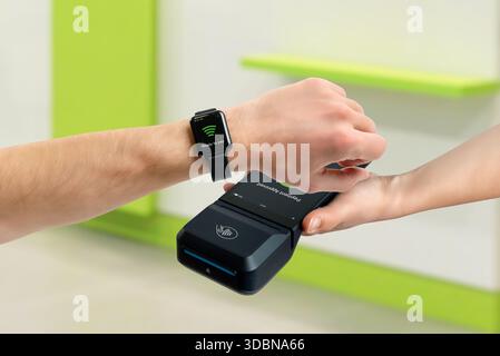 Kunden zahlen mit Smart Watch über kontaktloses POS-Terminal in Innenräumen, demonstrieren TAP-Zahlungen, tragbare Technologie, digitale Transaktionen und Modus Stockfoto