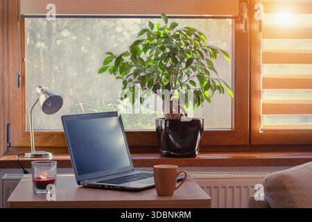 Arbeitsplatz zu Hause mit Laptop. Gemütliches Zuhause im warmen Fensterlicht durch Jalousien. Stockfoto