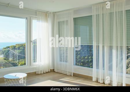 Gemütliches, helles Haus mit großen Fenstern, Jalousien und Vorhängen. Stockfoto