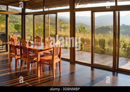 Holztisch im Inneren des Hauses. Große Glasfenster und Blick in die Landschaft. Stockfoto