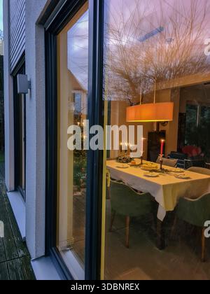 Blick von außen durch ein Fenster in ein festlich dekoriertes Wohnzimmer mit Weihnachtsbaum, festliche Dekoration im Essbereich Stockfoto