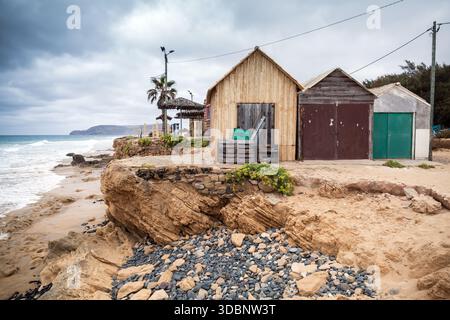 Verwitterte hölzerne Bootsscheunen sitzen an einer felsigen Küste unter einem bewölkten Himmel. Landschaft der Insel Porto Santo, Portugal Stockfoto