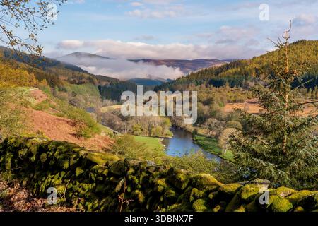 Ruhiger Fluss, der sich durch moosige Wände und sanfte Hügel in einer nebeligen schottischen Landschaft schlängelt. Stockfoto