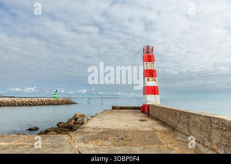 Blick auf den Leuchtturm Cais da Solaria am Praia da Batata in Lagos, Algarve, Portugal. Der rot-weiße Leuchtturm steht auf einem Betonpier mit Blick auf den Pier Stockfoto