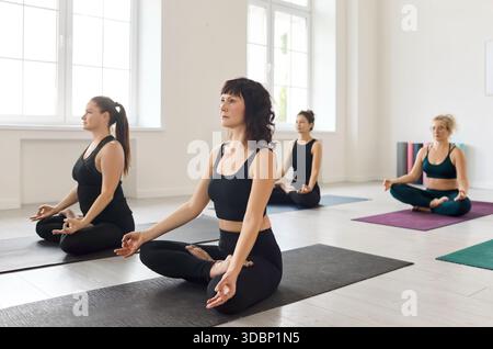 Frauen üben sitzende Yoga-Meditation im Lotus mit Mudras auf Studiomatten Stockfoto