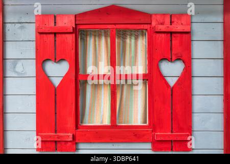 Rote Fensterläden aus Holz mit herzförmigen Ausschnitten an einer grauen Holzwand Stockfoto