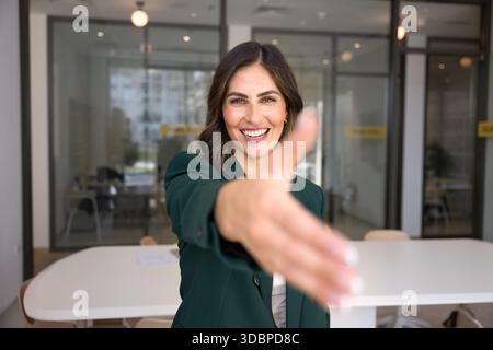 Glückliche, selbstbewusste hispanische Geschäftsfrau, die Hand für das Schütteln vor der Kamera gibt Stockfoto