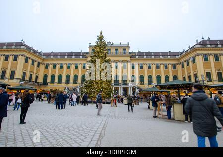 Die Leute spazieren und shoppen auf einem festlichen Weihnachtsmarkt mit Lichtern und Dekorationen vor einem großen historischen Gebäude mit Bogenfenstern Stockfoto