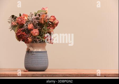 Ein minimalistisches Stillleben mit einem Blumenstrauß aus getrockneten Rosen und Wildblumen in einer handgefertigten Keramikvase. Auf einer rustikalen Holzoberfläche gegen Stockfoto