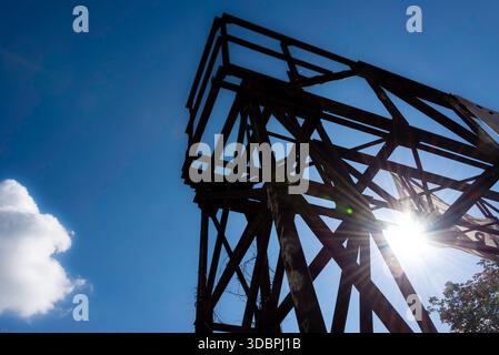 Dramatische flache Silhouette eines Stahlgitterturms vor einem tiefblauen Himmel mit einem hellen Sonnenaufgang. Industrielle Ästhetik bei Görlitzer P Stockfoto