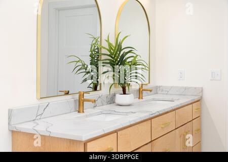 Ein modernes Badezimmer mit zwei Kosmetikflächen aus weißem Marmor mit goldenen Armaturen und bogenförmigen Spiegeln hängen über den Waschbecken. Stockfoto
