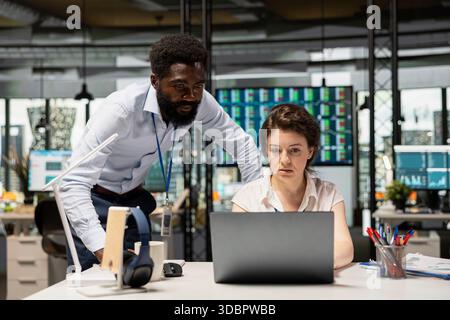 Multiethnische Kollegen diskutieren Projekte am Schreibtisch. Schwarze männliche Führungskraft und weibliche Angestellte verwenden Laptop auf dem Tisch, um Berichte zu analysieren, Statistiken zu verfolgen und Wachstumsstrategien für Unternehmen zu planen. Stockfoto