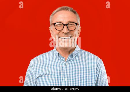 Mann lächelt vor rotem Hintergrund während eines ungezwungenen Moments in einer hellen Umgebung Stockfoto
