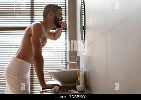 Gutaussehender junger arabischer Mann putzt Zähne im modernen Badezimmer während der Morgenroutine Stockfoto