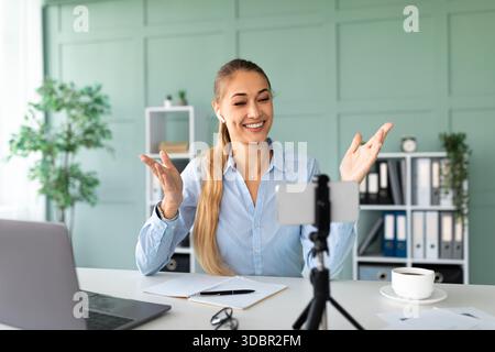 Happy Teacher führt von ihrem Office Workspace aus ansprechende Online-Lektionen mit Smartphone und Laptop durch Stockfoto