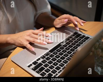 Frau, die einen Laptop an einem Café-Tisch benutzt, von der Seite gesehen Stockfoto