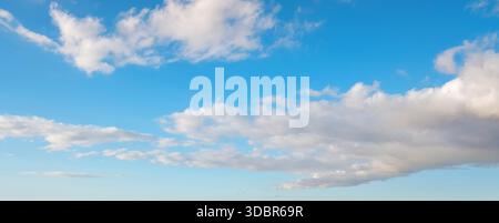Flauschige weiße Wolken ziehen an einem sonnigen Tag über einen hellblauen Himmel und schaffen eine beruhigende Aussicht. Stockfoto