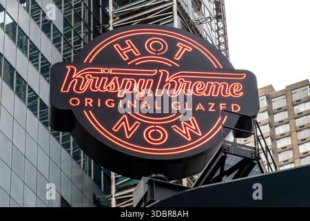 New York, NY - USA - 13. Dezember 2025 Ein großes, kreisförmiges Krispy Kreme-Schild am Times Square. Die roten Neonleuchten für „HEISS“ und „JETZT“ leuchten auf Stockfoto