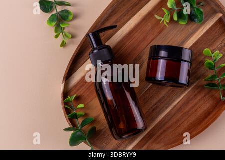 Pumpflasche aus braunem Glas und Glas auf Holztablett mit grüner Pflanze Stockfoto