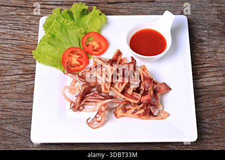 Frittierter sonnengetrockneter Tintenfisch auf einem weißen Teller Garnish mit Salat und Tomate Stockfoto