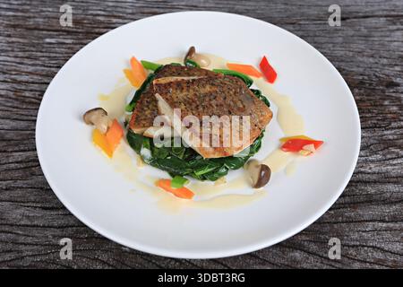 Seebarschsteak serviert mit Salat in Olivenöl und Zitronenscheiben auf Holztablett Stockfoto