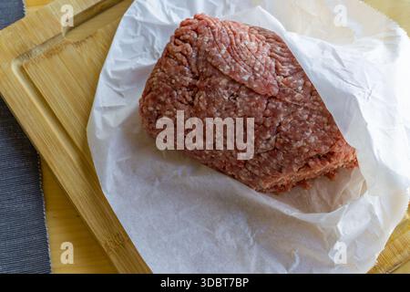 Rohes Hackfleisch/Faschiertes, gemahlenes Fleisch, frisches Fleisch, ungekochtes Rindfleisch, Kochzutat, Metzgerwaren, Fleischzubereitung, Pergamentpapier, Schneidebrett aus Holz, Stockfoto