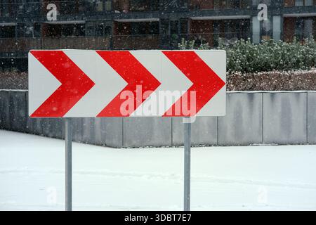 Vorderansicht eines rot-weißen, gewölbten Straßenschildes auf Metallpfosten, fotografiert in fallendem Schnee mit schneebedecktem Boden. Stockfoto
