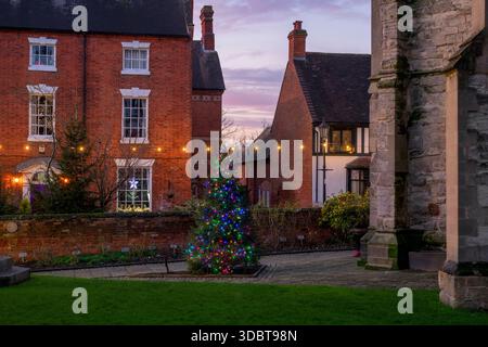 Weihnachtsbaum auf dem St. Nikolaus Kirchhof und dem Pfarrhaus entlang der Butterstraße in der Abenddämmerung im dezember. Alcester, Warwickshire, England Stockfoto