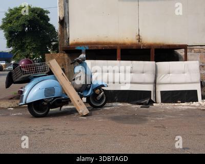 Ein klassisches blaues Retro-Motorrad im Vintage-Stil, das auf einem Seitenständer mit einem hinteren Korb in einer industriellen Umgebung geparkt ist. Stockfoto