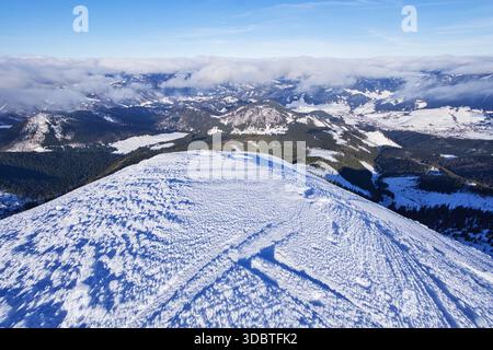 Blick auf einen schneebedeckten Berggipfel unter einem klaren blauen Himmel, im Kontrast zu den fernen Wolken und bewaldeten Tälern darunter, Nizke Tatry, Banska Bystr Stockfoto