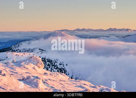 Blick auf schneebedeckte Gipfel durchdringen ein Meer aus ätherischen Wolken, geküsst vom warmen Schein der Dämmerung, und schaffen ein atemberaubendes Panorama, Kosarisko, Banska Stockfoto
