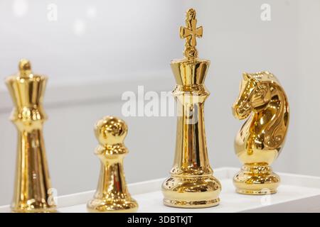 Eine Nahaufnahme von vier polierten goldenen Schachfiguren, darunter eine Königin, ein Bauernhof, ein König und ein Ritter, die auf einer weißen Oberfläche stehen Stockfoto