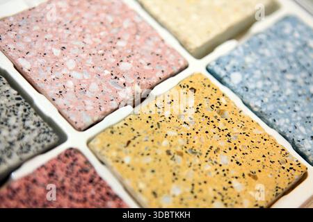 Eine von oben nach unten angewinkelte Nahaufnahme mehrerer quadratischer Terrazzo-Fliesen in verschiedenen Farben, einschließlich Rosa, Gelb, Blau und Grau, in einem weißen Tablett Stockfoto