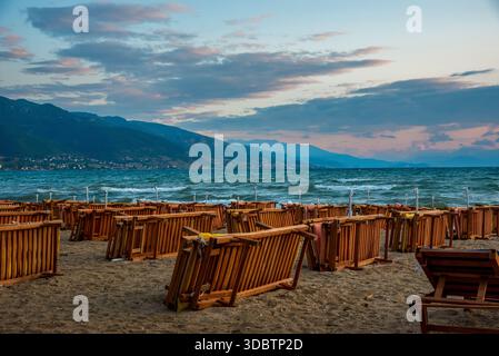 Leere Holzliegen am Lakeside Beach in der Abenddämmerung mit Bergkulisse Stockfoto